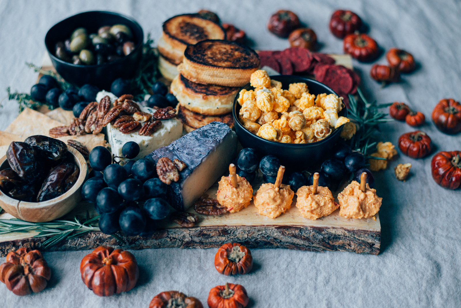 mini pimento cheese pumpkins on cheese board with maple glazed pecans, black grapes, olives, dates, and popcorn
