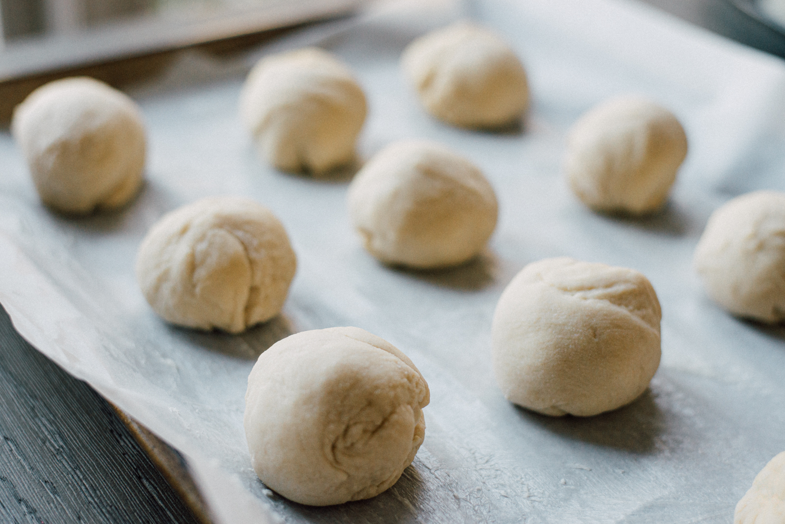 yeast dough parker house rolls in balls rising on parchment paper
