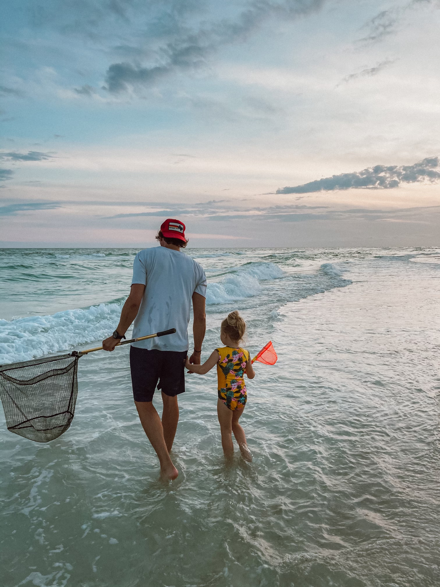 casey wiegand blog beach trip casey wiegand 30a house A family walking along the shore, kids in Seaside Swim swimsuits holding hands. The vertical stripe swimsuit drying on a beach chair in the sun.